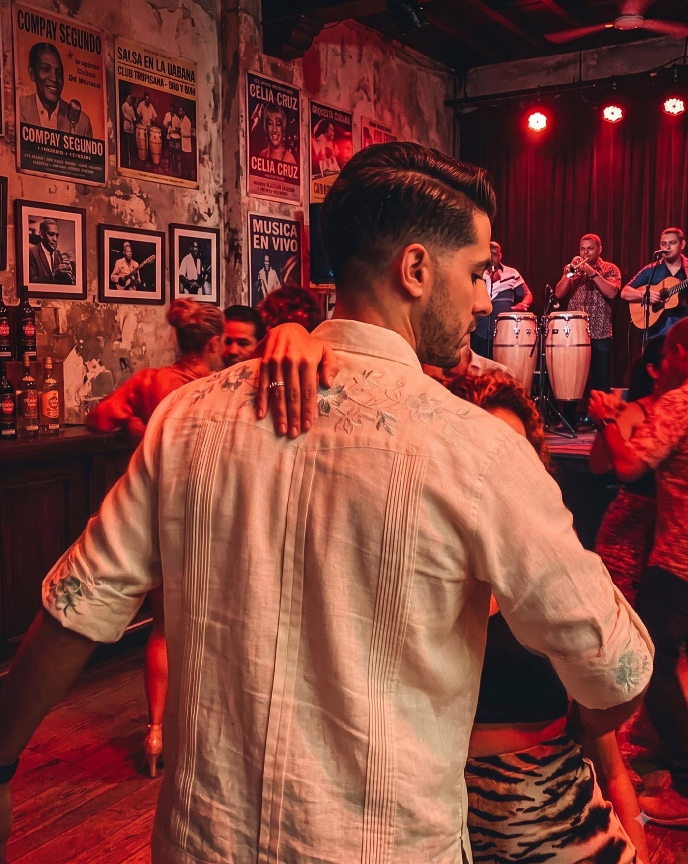 A couple dancing close on a crowded floor, her hand on his shoulder, lit deep red. Behind them a live band plays congas, trumpet and guitar, and the wall is covered in vintage Cuban music posters.